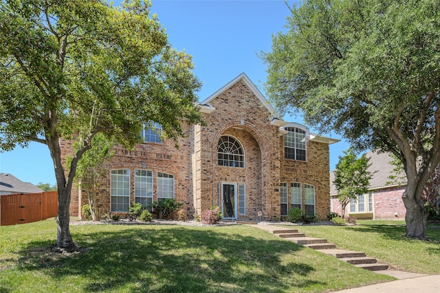 traditional-style home with brick siding, fence, and a front lawn