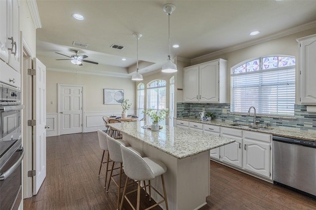 kitchen with stainless steel appliances, white cabinets, a sink, visible vents, and a kitchen breakfast bar