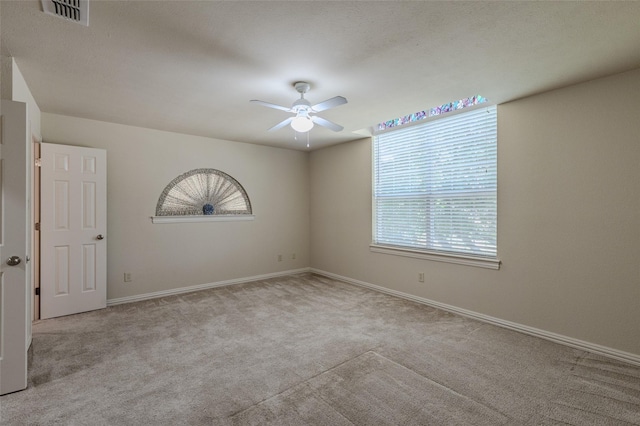 empty room featuring carpet flooring, a ceiling fan, visible vents, and baseboards