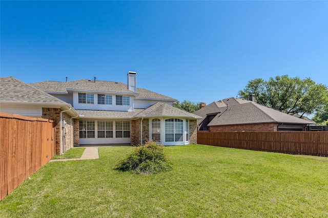 back of house featuring a yard, a chimney, a fenced backyard, brick siding, and roof with shingles