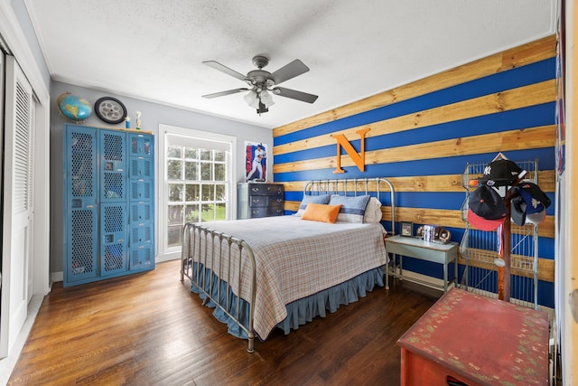 bedroom with wood walls, wood finished floors, a ceiling fan, a closet, and a textured ceiling