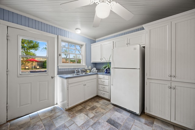 kitchen with a sink, stone tile floors, white cabinets, ornamental molding, and freestanding refrigerator