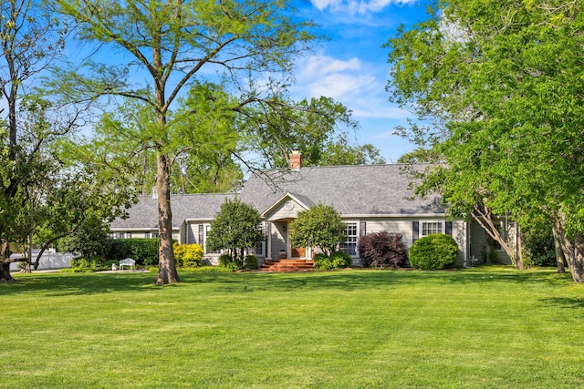 view of front of home with a shingled roof, a front lawn, and a chimney