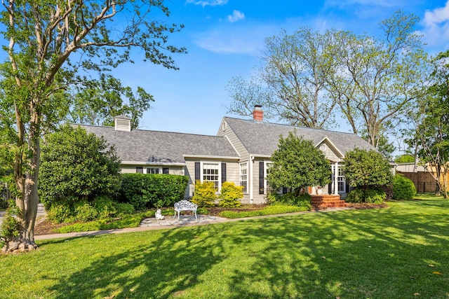 view of front facade featuring a chimney, a front yard, fence, and a shingled roof