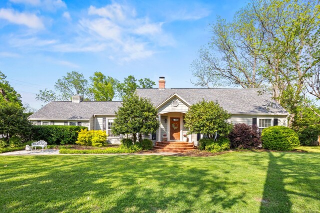 view of front facade featuring a chimney, a front lawn, and a shingled roof