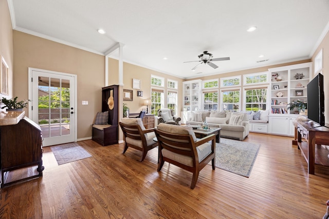 living area with light wood-type flooring, plenty of natural light, a ceiling fan, and crown molding