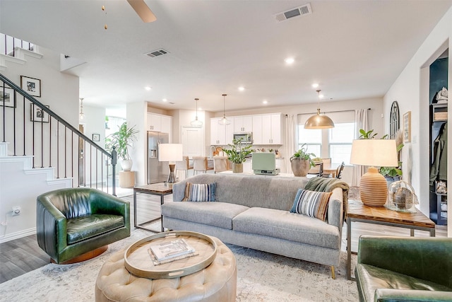living area with stairs, light wood finished floors, visible vents, and ceiling fan