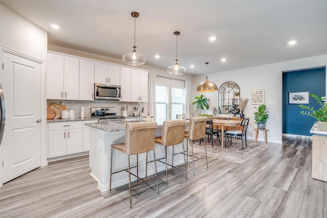 kitchen with white cabinetry, light wood-style flooring, appliances with stainless steel finishes, and a kitchen island with sink
