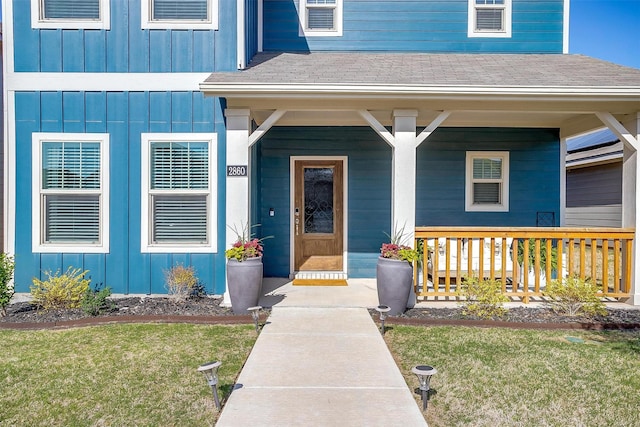 entrance to property featuring roof with shingles, board and batten siding, covered porch, and a yard
