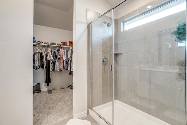 bathroom with a shower stall, a walk in closet, and baseboards