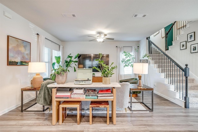 living room featuring light wood-style floors, a ceiling fan, visible vents, and stairs