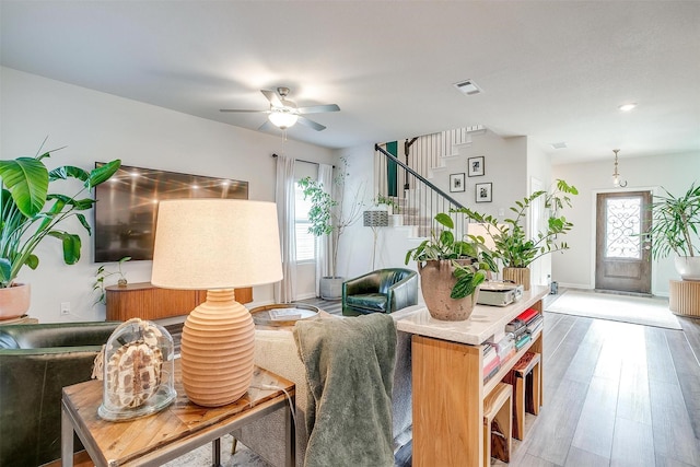 living area with visible vents, baseboards, a ceiling fan, wood finished floors, and stairs