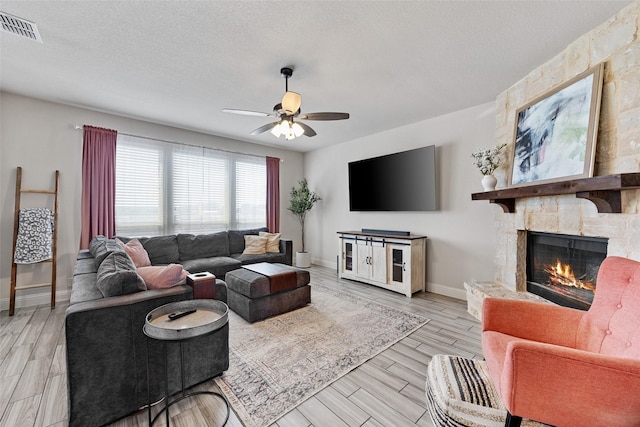 living room with a textured ceiling, visible vents, light wood finished floors, a fireplace, and a ceiling fan
