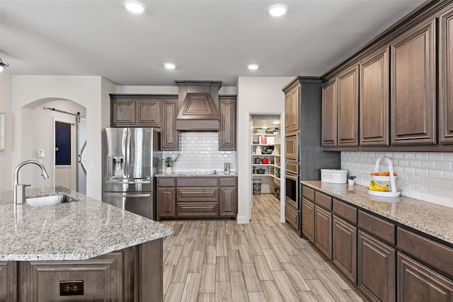 kitchen with a sink, a barn door, stainless steel appliances, custom exhaust hood, and backsplash