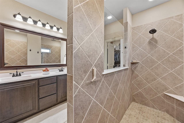 full bath with a spacious closet, tiled shower, double vanity, and a sink