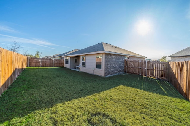 rear view of house with a yard, a fenced backyard, brick siding, and roof with shingles