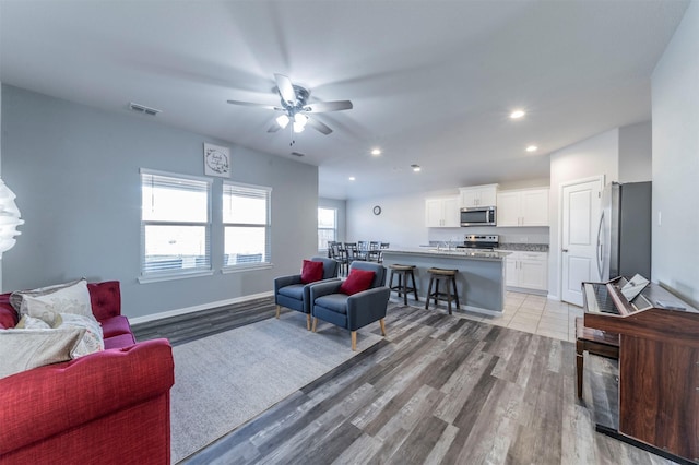 living area featuring a ceiling fan, visible vents, recessed lighting, light wood finished floors, and baseboards