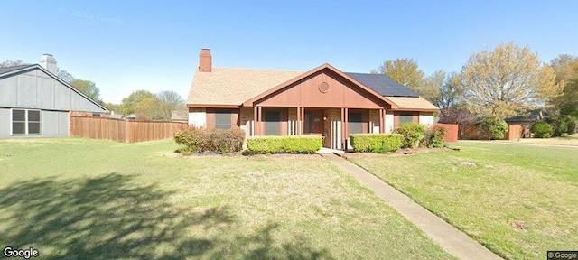 view of front of home with solar panels, a chimney, fence, and a front lawn