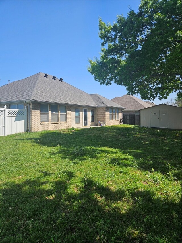 back of house featuring brick siding, fence, a yard, and a shed
