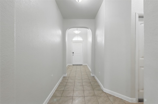 corridor with light tile patterned floors, baseboards, and arched walkways