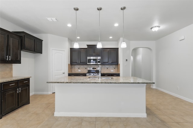 kitchen with arched walkways, light stone counters, decorative backsplash, and stainless steel appliances