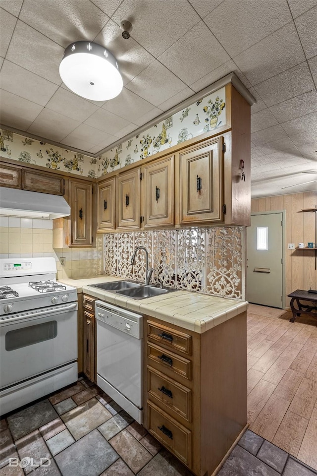 kitchen featuring a sink, white appliances, under cabinet range hood, tile counters, and decorative backsplash