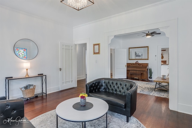 living room featuring ceiling fan with notable chandelier, baseboards, wood finished floors, and ornamental molding