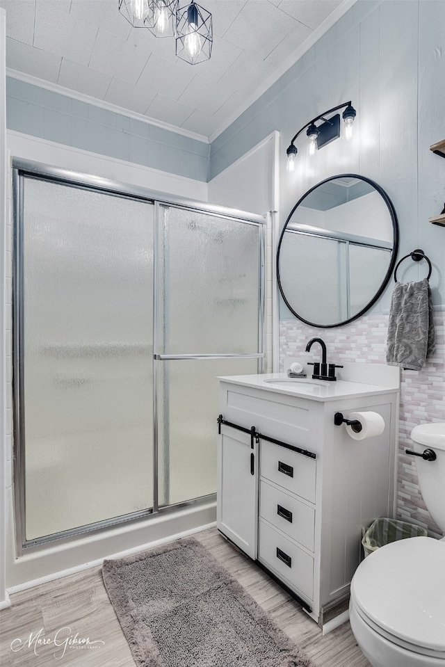 bathroom with wood finished floors, a shower stall, ornamental molding, and toilet
