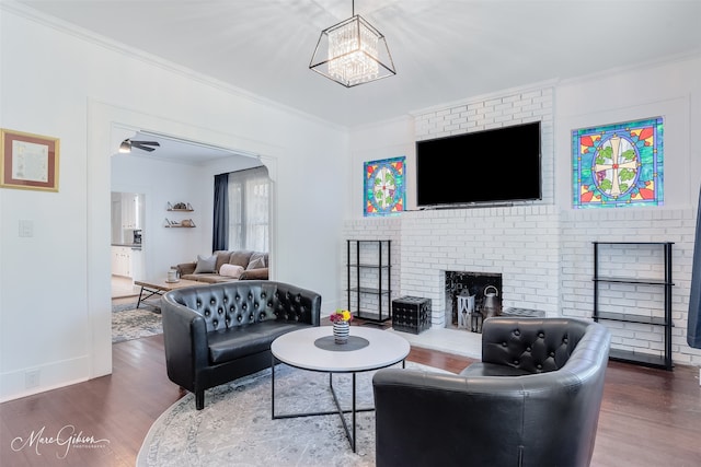 living room featuring baseboards, a chandelier, wood finished floors, a fireplace, and ornamental molding