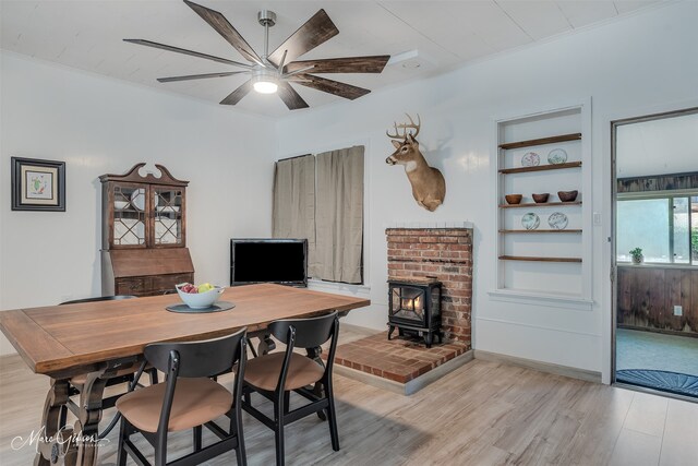 dining area featuring light wood finished floors, ceiling fan, built in shelves, and a wood stove