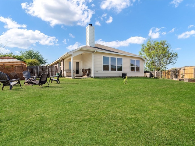 rear view of property featuring a fenced backyard, a fire pit, a chimney, and a lawn