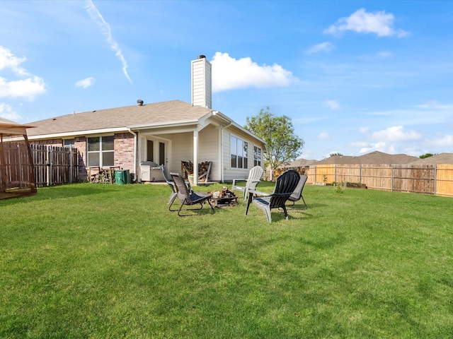rear view of property featuring a lawn, a fenced backyard, and an outdoor fire pit