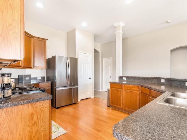 kitchen with light wood-type flooring, freestanding refrigerator, arched walkways, and a sink