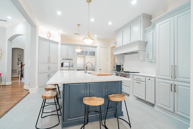 kitchen featuring a breakfast bar area, arched walkways, appliances with stainless steel finishes, light countertops, and ornamental molding