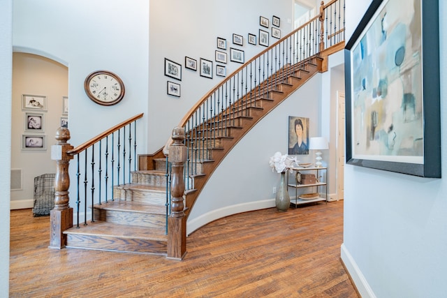 stairs featuring arched walkways, wood finished floors, a towering ceiling, and baseboards