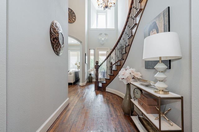 foyer entrance with stairs, hardwood / wood-style flooring, arched walkways, baseboards, and a notable chandelier