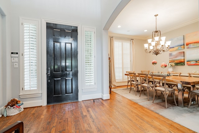 entrance foyer with crown molding, wood finished floors, arched walkways, baseboards, and a notable chandelier