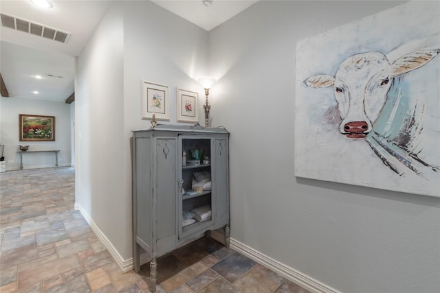 hall featuring baseboards, visible vents, and stone finish flooring