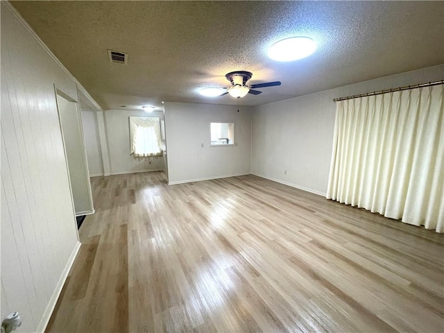 spare room with wood finished floors, a textured ceiling, ceiling fan, baseboards, and visible vents