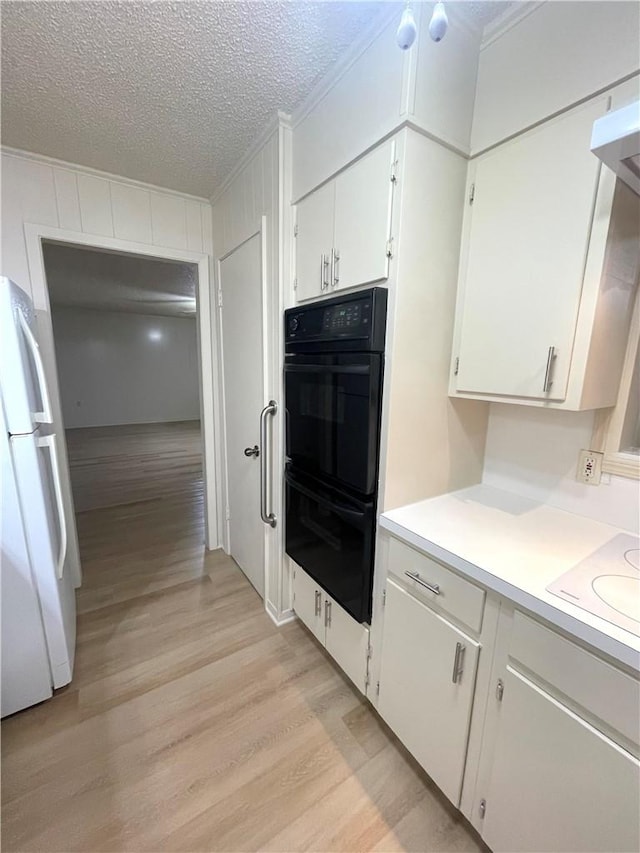 kitchen featuring dobule oven black, light wood finished floors, light countertops, ornamental molding, and freestanding refrigerator