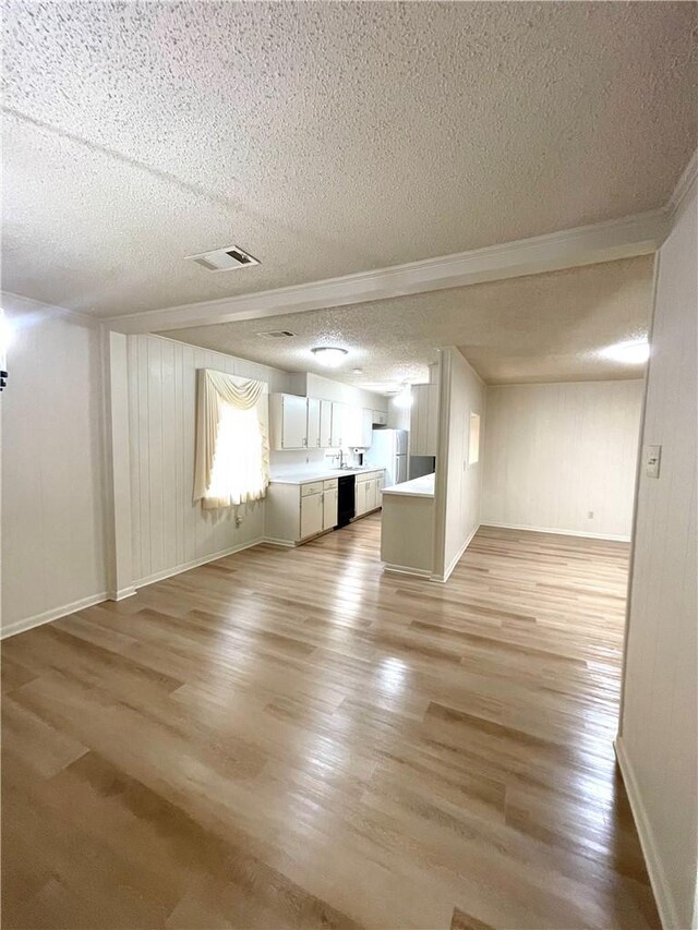 unfurnished living room with baseboards, light wood-style floors, visible vents, and a textured ceiling