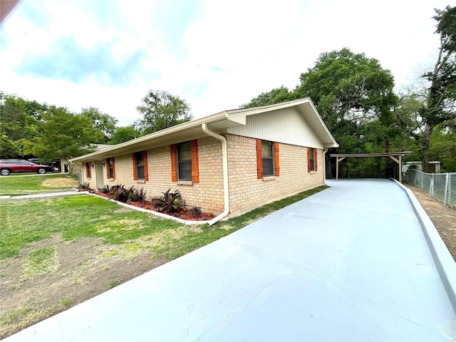 view of side of home featuring brick siding, a yard, driveway, and fence