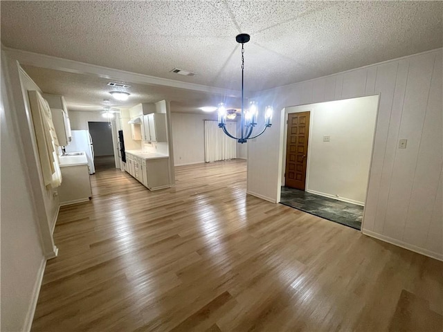 unfurnished dining area featuring wood finished floors, visible vents, baseboards, a textured ceiling, and a notable chandelier