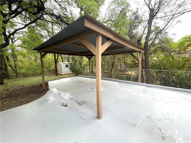 view of patio with a shed, driveway, an outdoor structure, fence, and a detached carport