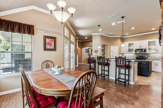 dining room featuring light wood-type flooring, baseboards, visible vents, and ornamental molding