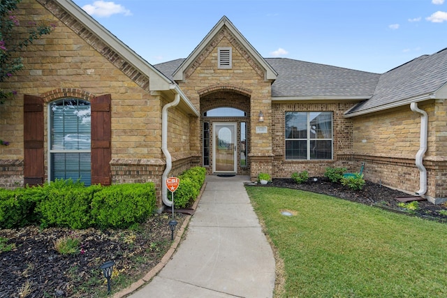 property entrance featuring a shingled roof, brick siding, and a yard
