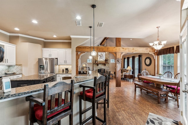 kitchen featuring stainless steel refrigerator with ice dispenser, dark stone countertops, a sink, and visible vents