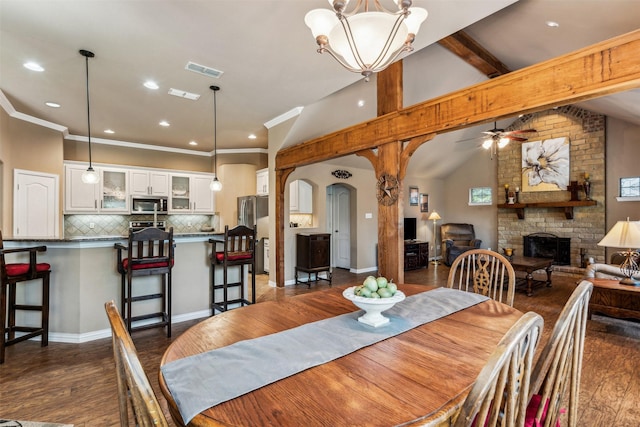 dining area featuring vaulted ceiling with beams, arched walkways, visible vents, a brick fireplace, and dark wood-style floors