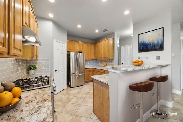 kitchen featuring decorative backsplash, a breakfast bar area, appliances with stainless steel finishes, under cabinet range hood, and visible vents