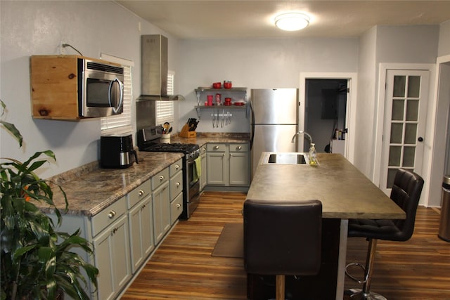 kitchen with wall chimney range hood, stainless steel appliances, dark wood-style floors, and a sink